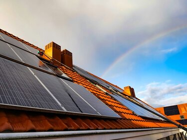 Sicherer Notstrom mit Solaranlagen auf Balkon oder Dach Dach eines Einfamilienhauses mit Solarpaneelen, über das sich ein Regenbogen neigt