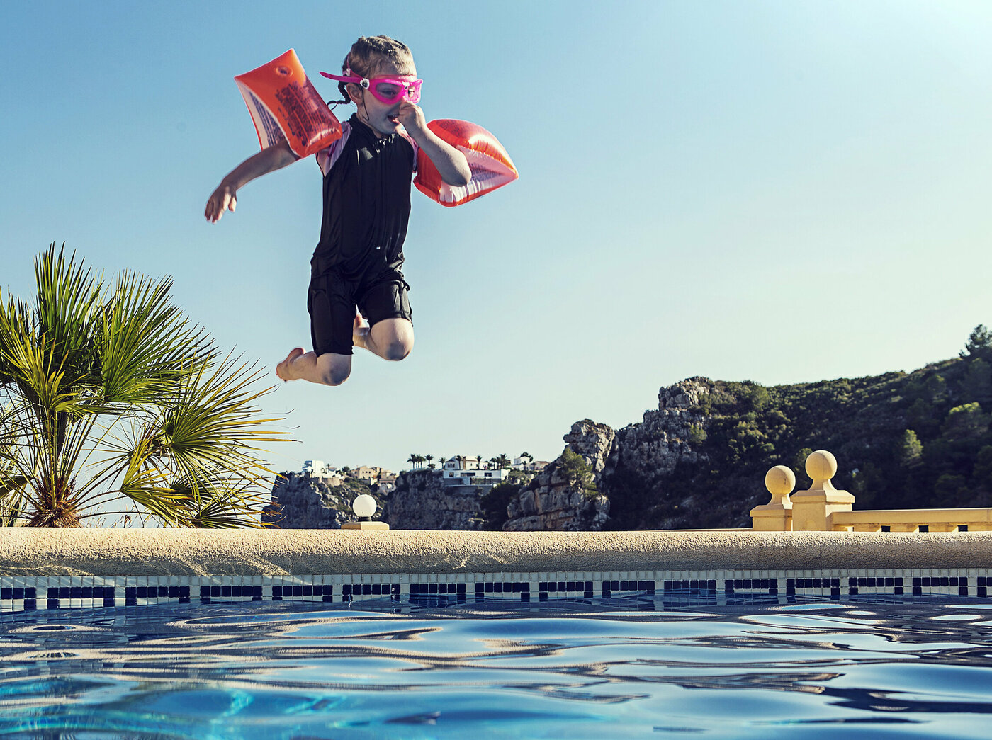 Ein Kind mit Schwimmflügeln springt an einem Strand ins Wasser
